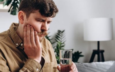 Close up of sad young man feel terrible toothache after drink cold water. Male 30s sitting on sofa at home touching cheek, feel hurt and suffering from sensitive tooth ache. Pain and cavities concept